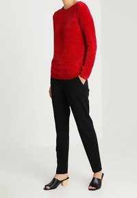 Červený svetr s dlouhými rukávy, doplněný černými zúženými kalhotami a černými otevřenými sandály na dřevěných podpatcích.