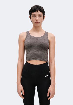 Ung kvinde med kort mørkt hår iført en ærmeløs grå crop top og sorte leggings med høj talje med et lille hvidt logo.