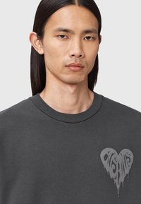 Mørkegrå sweatshirt med rund hals og en hjerteformet grafik i lysegrå med et dryppende design på venstre brystområde.