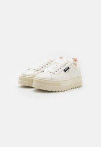 Zapatillas de cuero blancas con suela de plataforma texturizada, punta redonda y acentos beige contrastantes en el talón. Presenta una etiqueta de logo en el lateral.