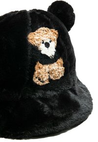 Sombrero tipo bucket de piel sintética negra con un diseño de oso bordado en marrón y blanco. Parte superior redondeada con detalles juguetones de pompones.