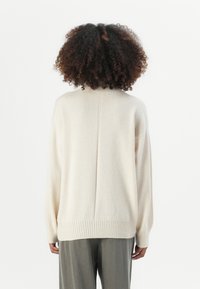 Cremfarbener, übergroßer Pullover aus weichem Material, mit geripptem Saum und Bündchen, der eine zentrale Naht am Rücken aufweist.