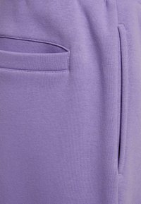 Fioletowe dresy wykonane z gładkiego materiału, z boczną kieszenią i elastycznym pasem z troczkiem do regulacji dopasowania.