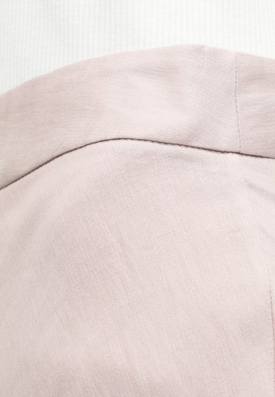 Κοντινό πλάνο σε μπεζ ύφασμα που δείχνει λεπτομερή ραφή και υφή, εστιάζοντας στη καμπυλωτή ραφή και την ομαλή επιφάνεια του υλικού.