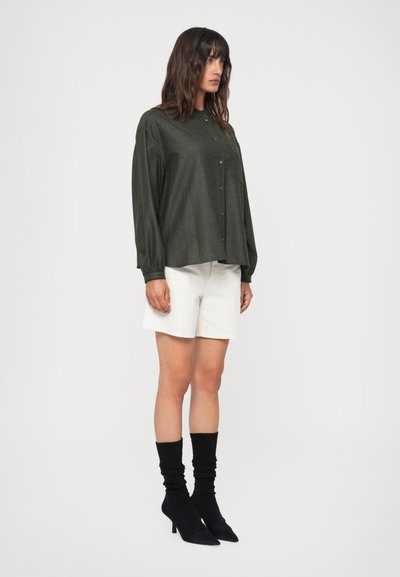 Camasa butonată de culoare verde închis, cu mâneci lungi, asortată cu pantaloni scurți albi. Ciorapi negri până la glezne și pantofi cu vârful ascuțit completează ținuta.