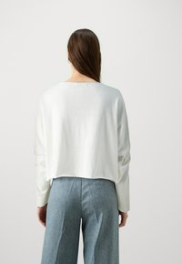 Hvit, kortermet topp med lang erm og rund hals, som har en glatt tekstur. Kombinert med lyseblå vide bukser i denimstoff.