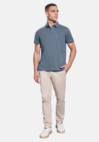 Kortärmad pikétröja i skifferblå, bomullsblandning, med en treknapplikning och en subtil logotyp. Matchad med ljusbeige byxor och vita sneakers.