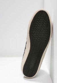 Černá podešev tenisky s texturovaným, vlnitým vzorem a střední částí v krémové barvě. Na spodní straně je vyražené logo "GEOX". Čistý, minimalistický design.