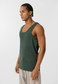 Groene geribbelde tanktop met een relaxte pasvorm, ruwe randen en brede armsgaten, gecombineerd met lichtgekleurde, losvallende broeken.