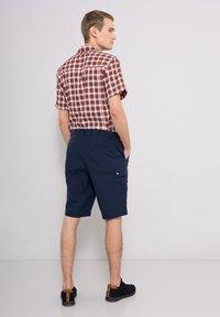 Brun och beige rutigt kortärmat skjorta, ihop med marinblå shorts med sidofickor och en texturerad yta. Svarta skor med bruna detaljer.