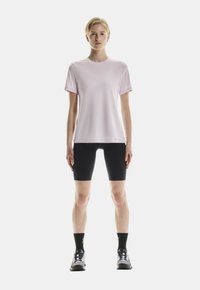 Helles rosa T-Shirt mit kurzen Ärmeln, kombiniert mit schwarzen Radlerhosen, schwarzen Socken und grauen Sportschuhen. Einfaches Design, minimale Details.