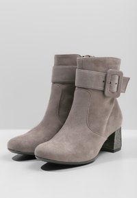 Botines de ante gris con una amplia correa y detalle de hebilla, con un tacón de bloque negro texturizado y punta redondeada y lisa. Cierre de cremallera lateral.