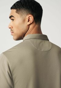 Khakifarbene, strukturierte Hemd mit Kragen, das ein dezentes geometrisches Muster aufweist, eine taillierte Silhouette zeigt und glatte Stoffdetails bietet.