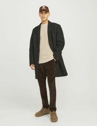 Cappotto nero, maglione beige a texture, pantaloni in corduroy marroni e scarpe marroni stringate. Cappello marrone con dettaglio del logo. Estetica semplice e moderna.