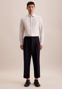 Witte lange mouwen blouse met kraag, gecombineerd met marineblauwe geplooide broek en zwarte veterschoenen. Effen textuur, slim fit.