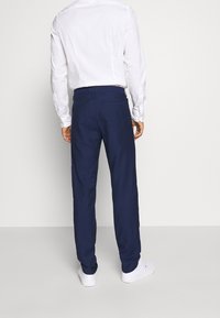 Pantaloni blu realizzati in tessuto texturizzato, con un design a gamba dritta, passanti per la cintura e tasche posteriori, abbinati a una camicia bianca.