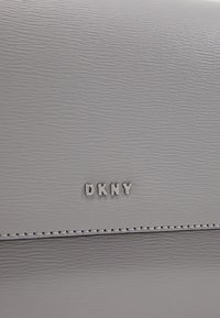 Šedá texturovaná kožená kabelka s výrazným stříbrným logem "DKNY". Obsahuje prošívané detaily podél okraje. Kompaktí obdélníkový design.