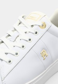 Baskets en cuir blanc avec lacets blancs, logo doré sur le côté et œillets dorés, vues en gros plan.