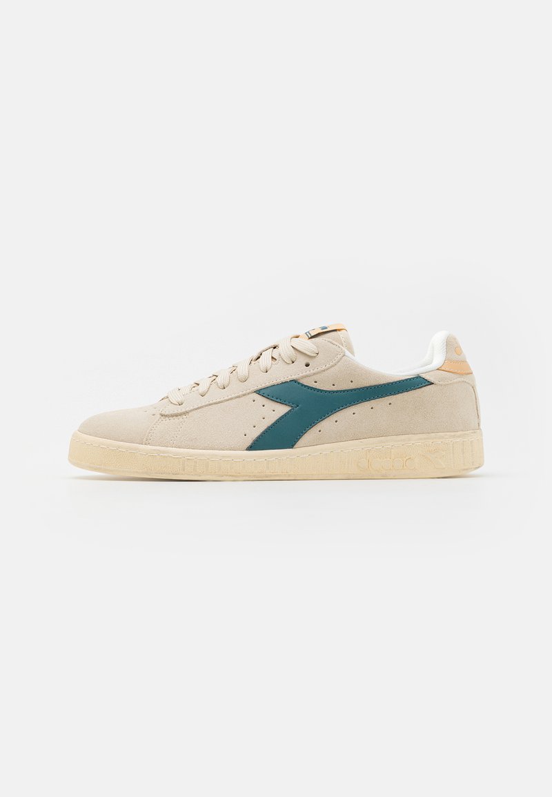 Beige suede sneakers with teal accents, round toe, lace-up closure, and textured rubber sole. Small logo on the side and heel.