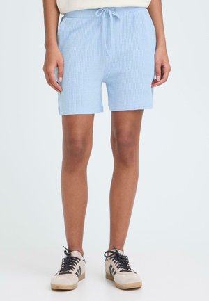 Shorts en coton côtelé bleu clair avec une taille élastique et un cordon de serrage. Portés avec des baskets beige à rayures noires.