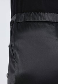 Černá saténová látka s hladkým povrchem, vybavená elastickým pasem a dekorativními stříbrnými akcenty po stranách.