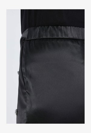 Black satin fabric with a smooth texture, featuring an elastic waistband and decorative silver accents along the side.