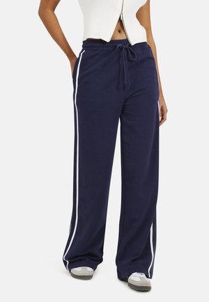 Pantaloni della tuta blu navy con vita regolabile, strisce bianche sui lati e vestibilità ampia. Realizzati in tessuto morbido, con tasche senza cuciture sui lati.