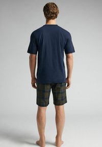 Mörkblå bomulls-T-shirt i kombination med rutiga shorts i grön, mörkblå och gul. Shorts har en klassisk passform och en fåll som slutar ovan knäna.