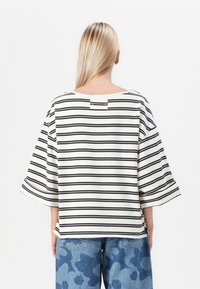 Stripet bomulls topp med vide ermer, som har svart og hvit horisontale striper, en avslappet passform, og en lukking på baksiden.