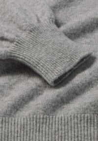 Detail van een grijze gebreide trui, met een geribbelde manchet en een gladde lichaamstructuur, die zacht wolmateriaal met subtiele kleurvariatie toont.