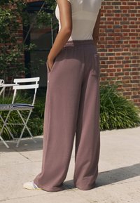 Pantaloni largi, cu talie înaltă, din bumbac de culoare mov deschis, având buzunare laterale și un logo discret. Purtați cu adidași deschiși la culoare.