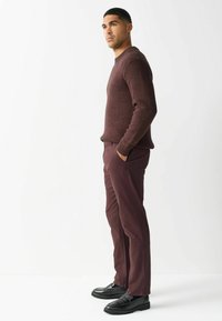 Pulover tricotat cojociu, cu model texturat, asortat cu pantaloni slim-fit bordeaux și loafers negri, creând o schemă de culori coerentă.