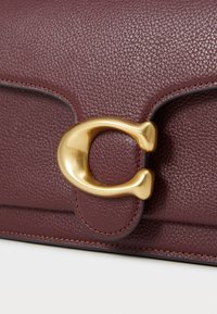 Burgundy leather handbag featuring a prominent gold-tone metal clasp and textured surface with visible stitching details.