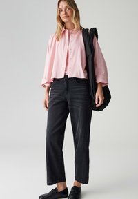 Light pink, long-sleeve, button-up shirt over a matching top; paired with dark denim jeans and black shoes; casual look, relaxed fit.