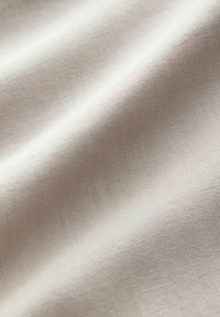 Lichtbeige stof met een gladde textuur en een subtiel geweven patroon. Het oppervlak toont fijne, gelijkmatige nerfstructuren, wat de natuurlijke uitstraling versterkt.