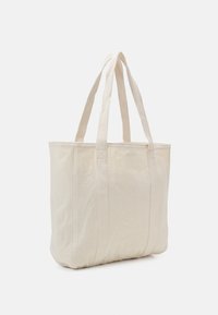 Cotton tote bag in cream color, featuring two long handles, a boxy shape, and reinforced seams for durability. Simple, unadorned design.