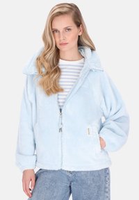 Jachetă din fleece albastru deschis cu fermoar frontal, guler mare și buzunare laterale. Croială supradimensionată cu textură moale, asortată cu un tricou în dungi pe dedesubt.