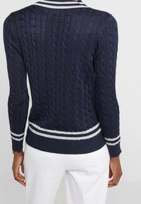 Granatowy sweter z warkoczowym splotem, z teksturowanym wzorem, featuring białymi paskami na kołnierzyku i mankietach. Dopasowany krój z długimi rękawami.