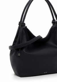 Melnas teksturētas ādas rokassomas ar dubultajiem rokturiem, sānu siksnu un sudraba krāsas metāla akcentu, kas atrodas uz baltas virsmas.