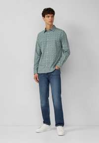Chemise button-up verte à motifs avec des manches longues, associée à un jean bleu et des baskets blanches. Design simple et coupe décontractée.