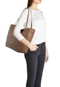 Borsa tote in pelle marrone con finitura testurizzata, dotata di doppi manici e design minimalista. Modello che la tiene in mano su uno sfondo bianco.