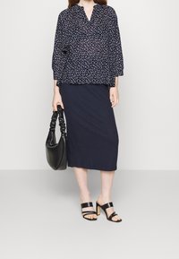 Blusa floreale navy con scollatura a V e maniche a tre quarti, abbinata a una gonna rigata navy. Borsa nera e sandali con tacco cubano.