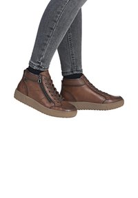 Baskets montantes en cuir brun avec une surface textur�ée, fermeture éclair latérale et semelle en caoutchouc, associées à un jean slim gris foncé.