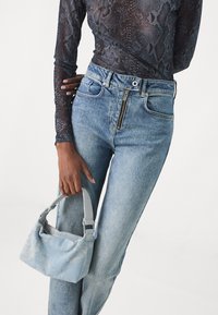 Blauwe denim jeans met een hoge taille en ritsluiting, gecombineerd met een zwart slangenprint lange mouwen top en een kleine lichtblauwe handtas.