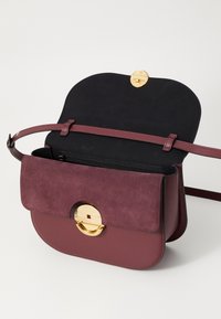 Borsa bordeaux in pelle e suede, con forma arrotondata, hardware circolare dorato e scomparto interno con zip.