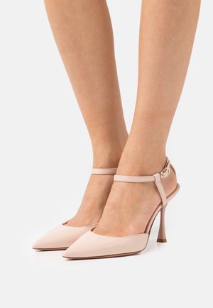 Chaussures à talons hauts rose pâle avec bout pointu, bride à la cheville et talon fin, présentant une finition brillante et un accent subtil de métal.
