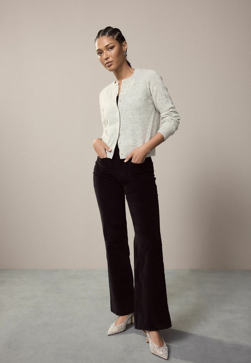 Šviesiai pilkas kardiganas su dėmėtu tekstūru, juodos prigludusios kelnės ir siauri priekyje bateliai su deimantų akcentais. Paprastas dizainas ir pritaikyta forma.