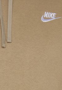 Karamelīgā krāsā svītrojums ar teksturētu virsmu, ar balto Nike logo augšējā labajā stūrī. Tam ir atbilstoši auklas kapuces atvēršanai.