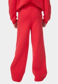 Røde, brede sweatpants lavet af blødt stof med elastisk talje. Har en glat tekstur og et minimalistisk design.