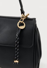 Czarna skórzana torebka o strukturalnym kształcie, z złotymi elementami i dekoracyjnym czarno-białym frędzlem z złotymi akcentami.